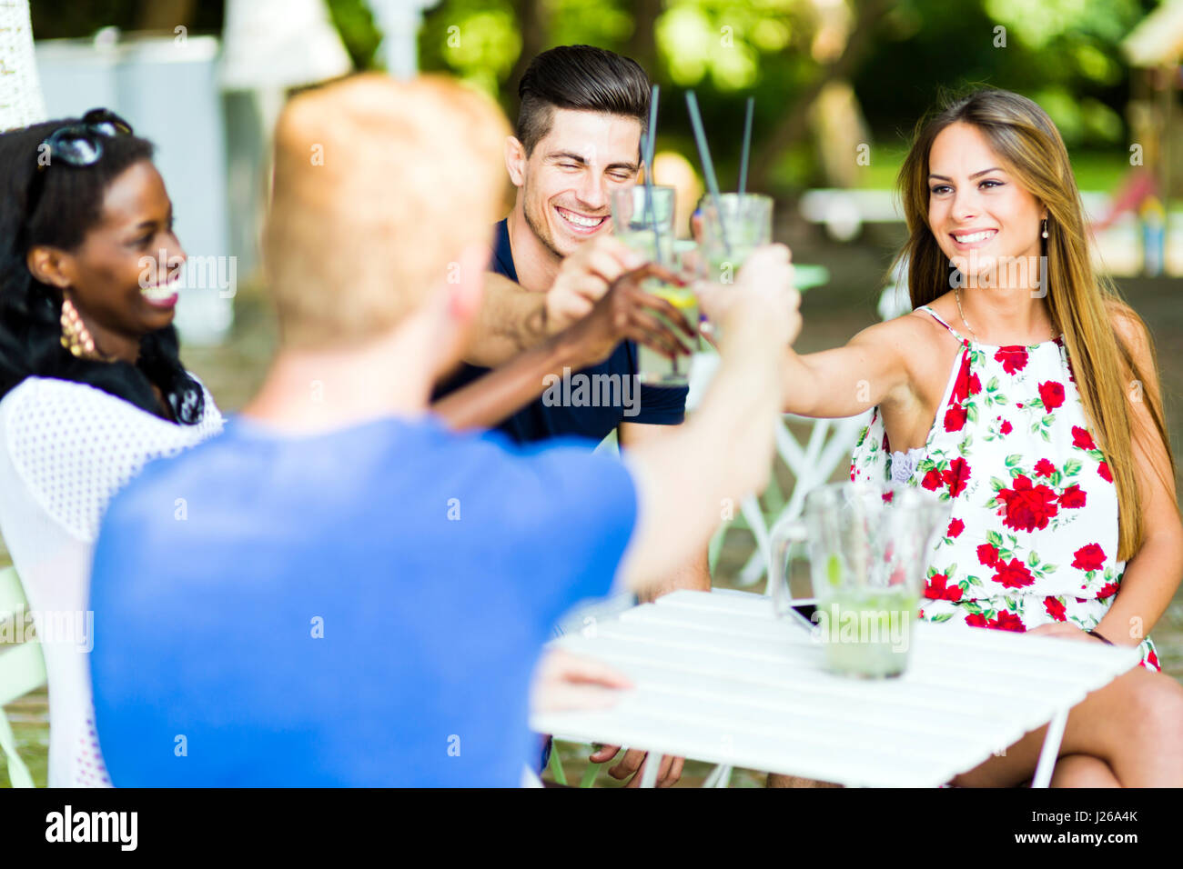 Il gruppo di allegro felici le persone la tostatura seduti ad un tavolo all'aperto in una calda giornata estiva Foto Stock