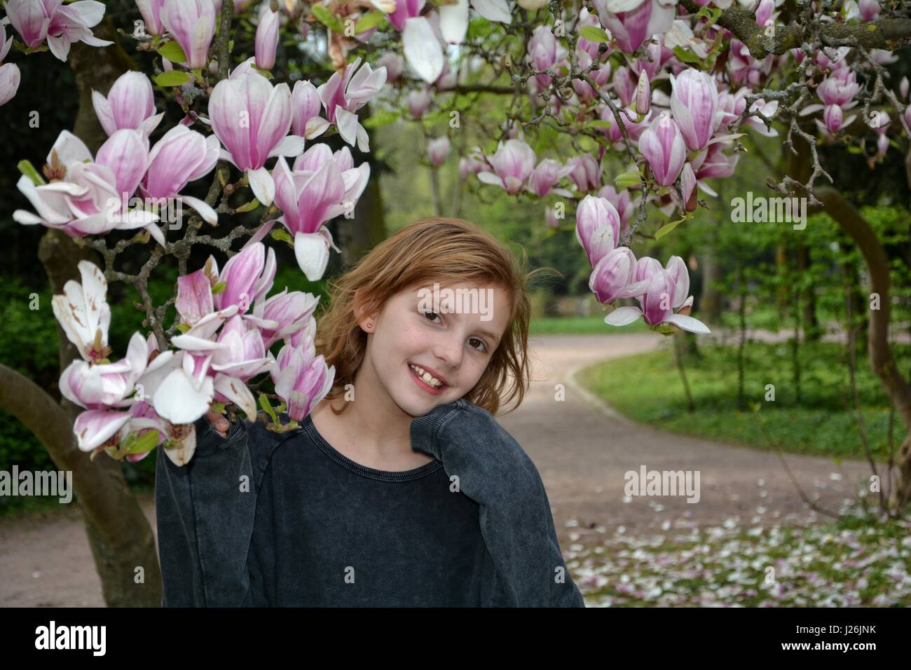 Ragazza dei cavalletti sotto la fioritura degli alberi di magnolia ( della Magnoliacee ) e risate in avanti, la mano sotto il mento Foto Stock