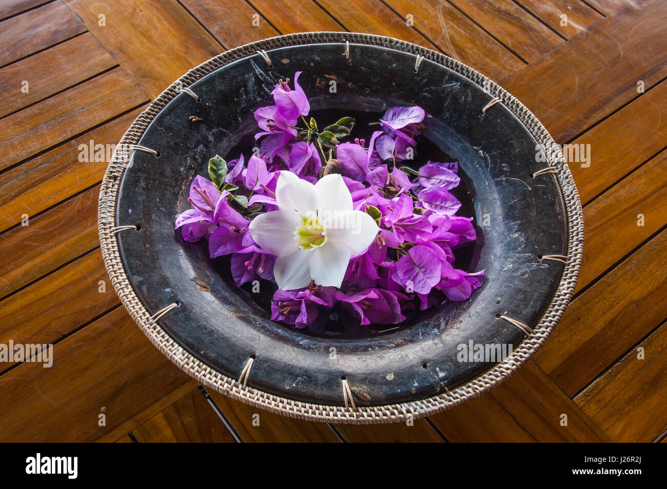 Artigianale di pentola di coccio con tessuto edge contiene una raccolta di calmante di fiori viola e un bellissimo fiore bianco, tutti su una base di doghe in teak Foto Stock
