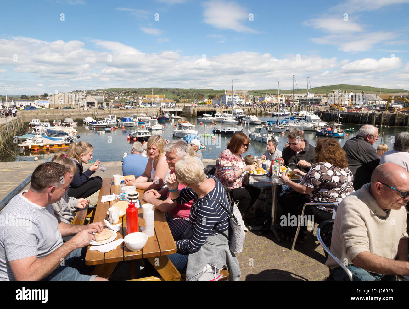 Una folla di gente che mangiare al caffè in una giornata di sole, West Bay Harbor, West Bay, Dorset England Regno Unito Foto Stock