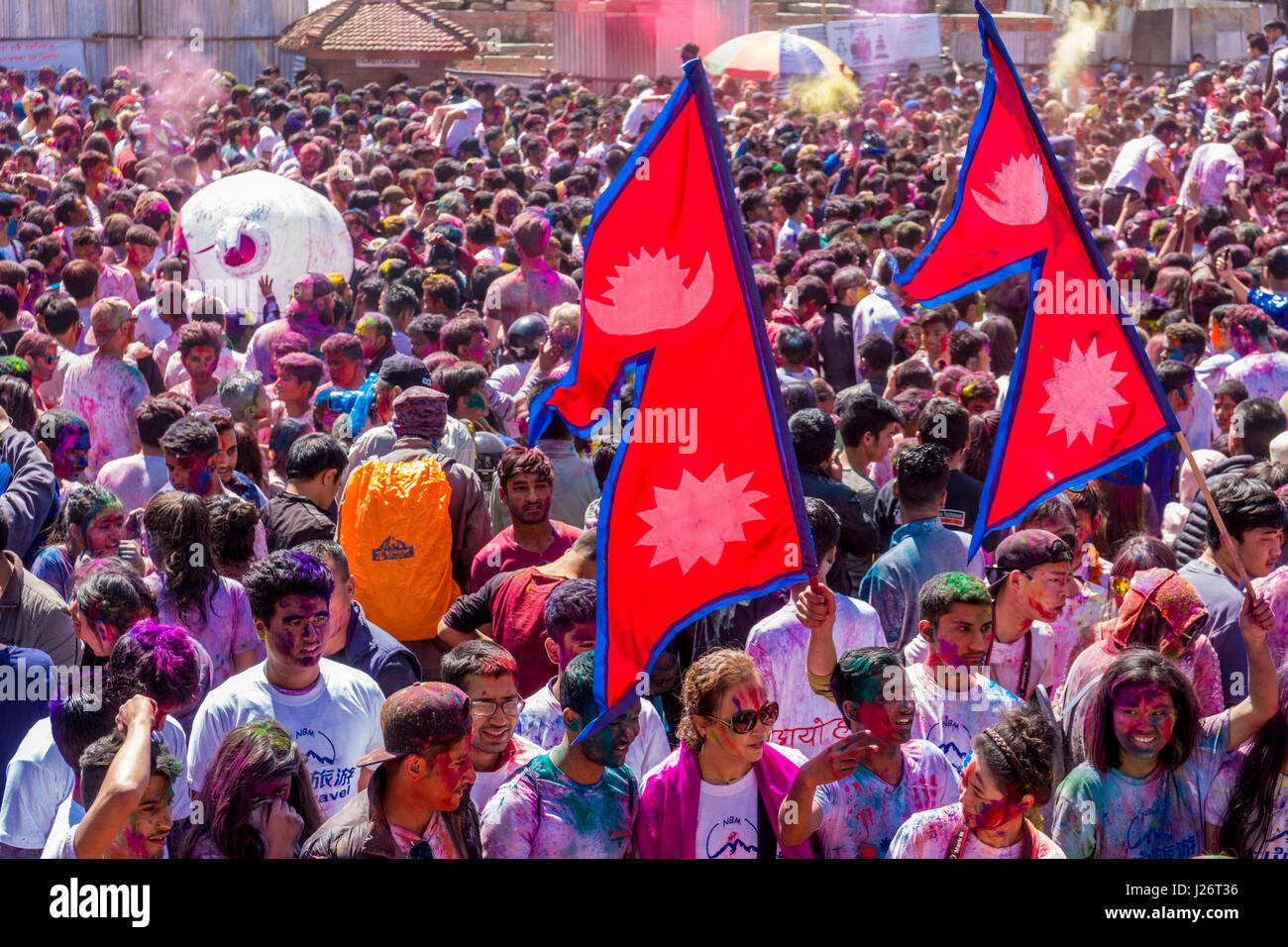 Migliaia di giovani, cosparse e a giocare con i colori, celebrano la Holi festival e agitando il nepalese bandiera nazionale Foto Stock