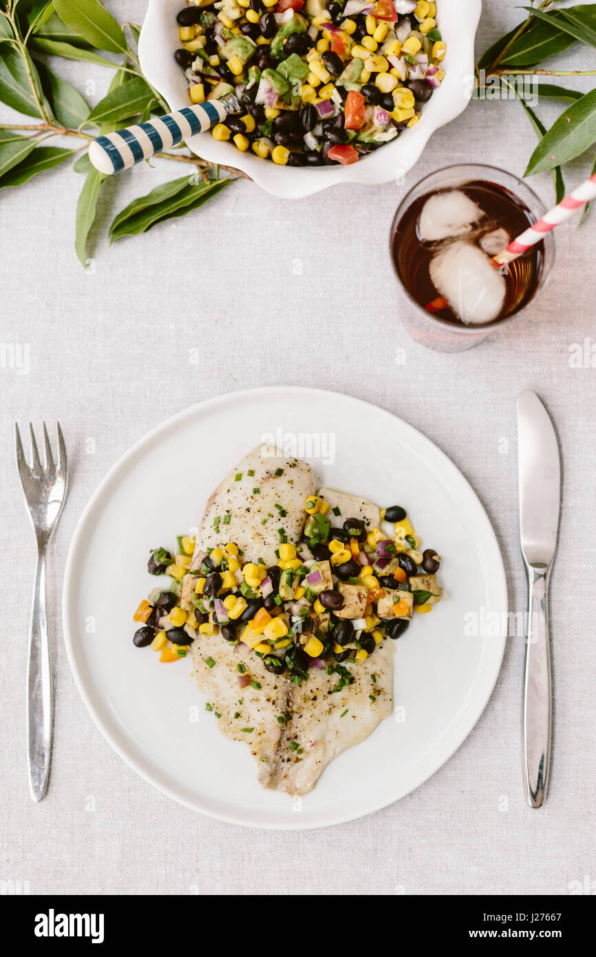 Due piastre di pane appena sfornato, tilapia condito con chicco nero salsa vengono fotografate su un tablesetting estivo. Foto Stock