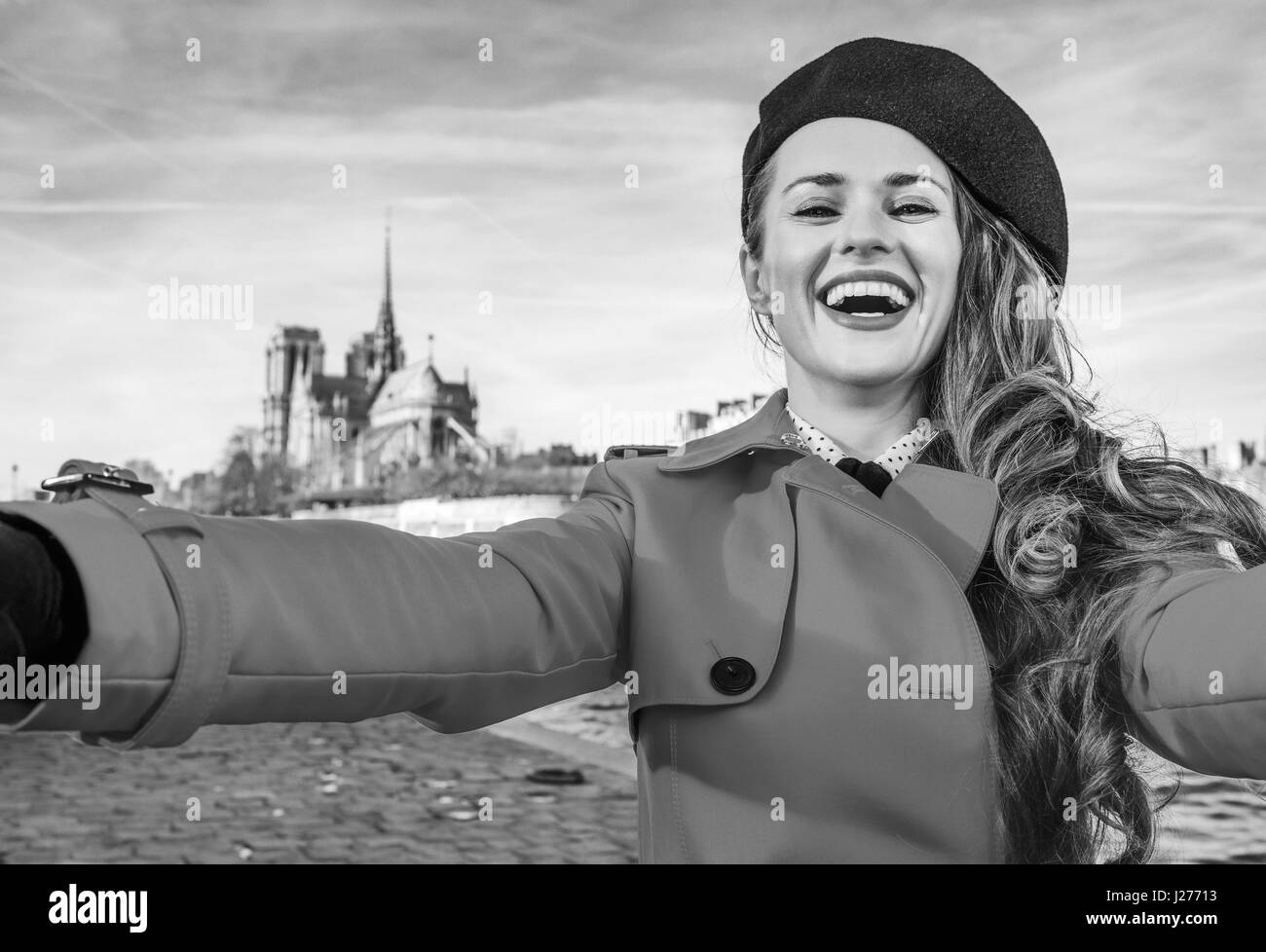 Luminose a Parigi. sorridente donna elegante in rosso trench coat sul terrapieno in Parigi, Francia tenendo selfie Foto Stock