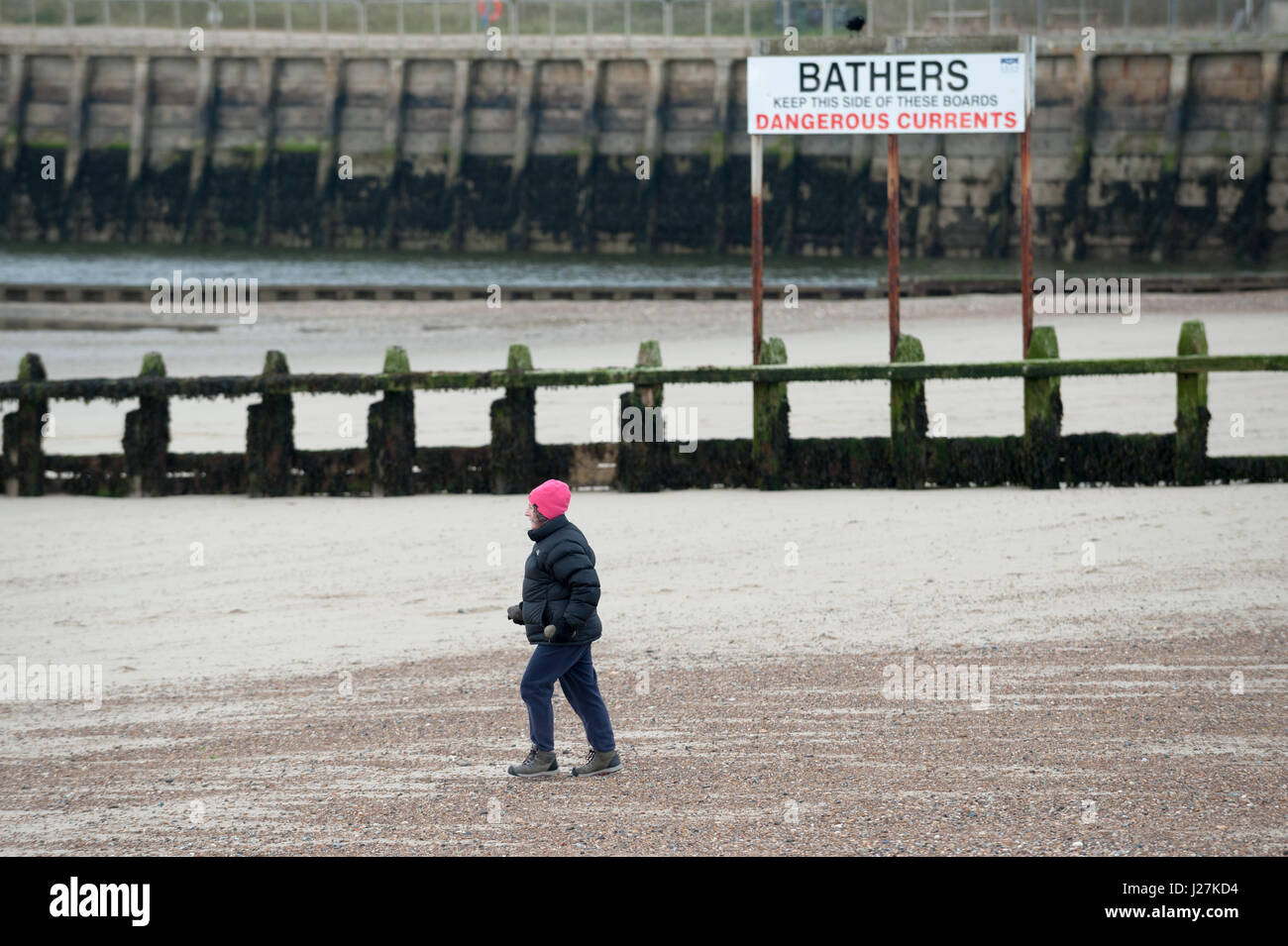 Una donna che indossa una giacca calda, un cappellino e guanti a piedi lungo la spiaggia in un freddo giorno di Littlehampton West Sussex, in Inghilterra. Foto Stock