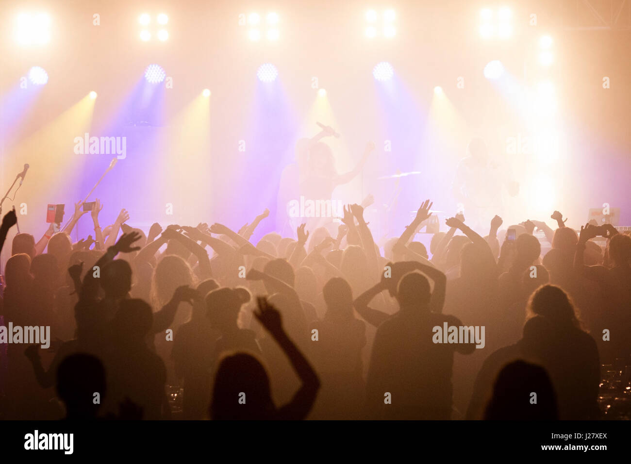 Udienza con le mani sollevate a un festival di musica e luci streaming verso il basso a partire da sopra il palcoscenico. Soft focus, ISO elevata, immagini sgranate. Foto Stock