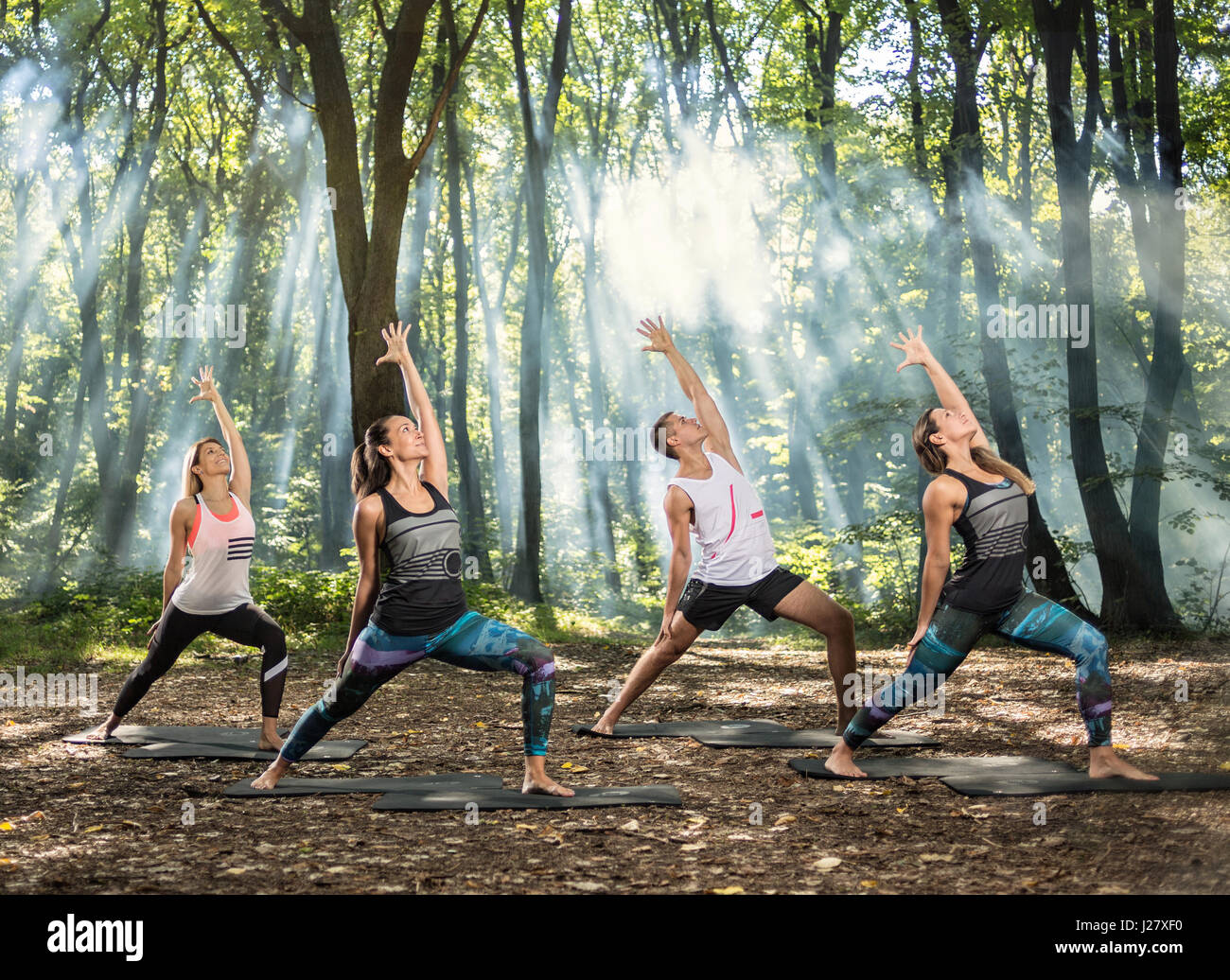 Un gruppo di giovani di eseguire semplici esercizi di stretching in sun foresta illuminata Foto Stock