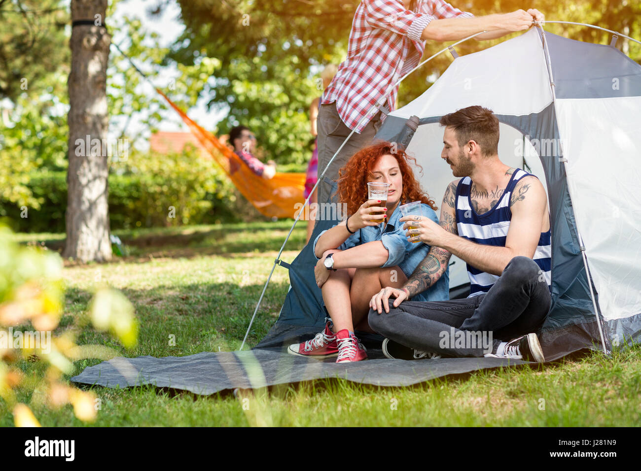 Maschio e femmina in estate bevande birra nella parte anteriore della tenda in foresta Foto Stock