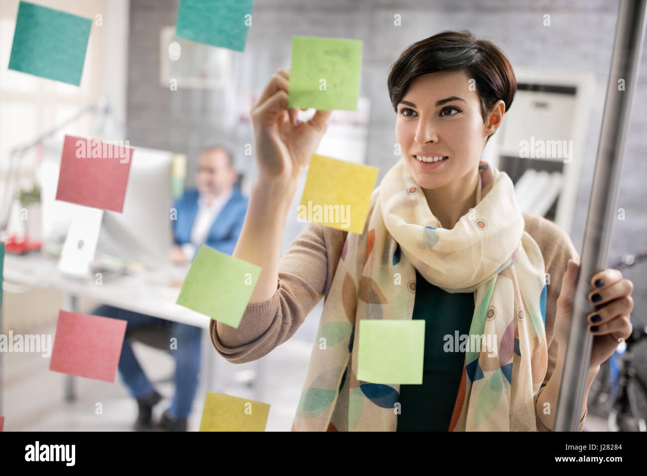 Moderna donna di lavoro fa di regime in adesivi sul pannello di vetro al posto di lavoro Foto Stock