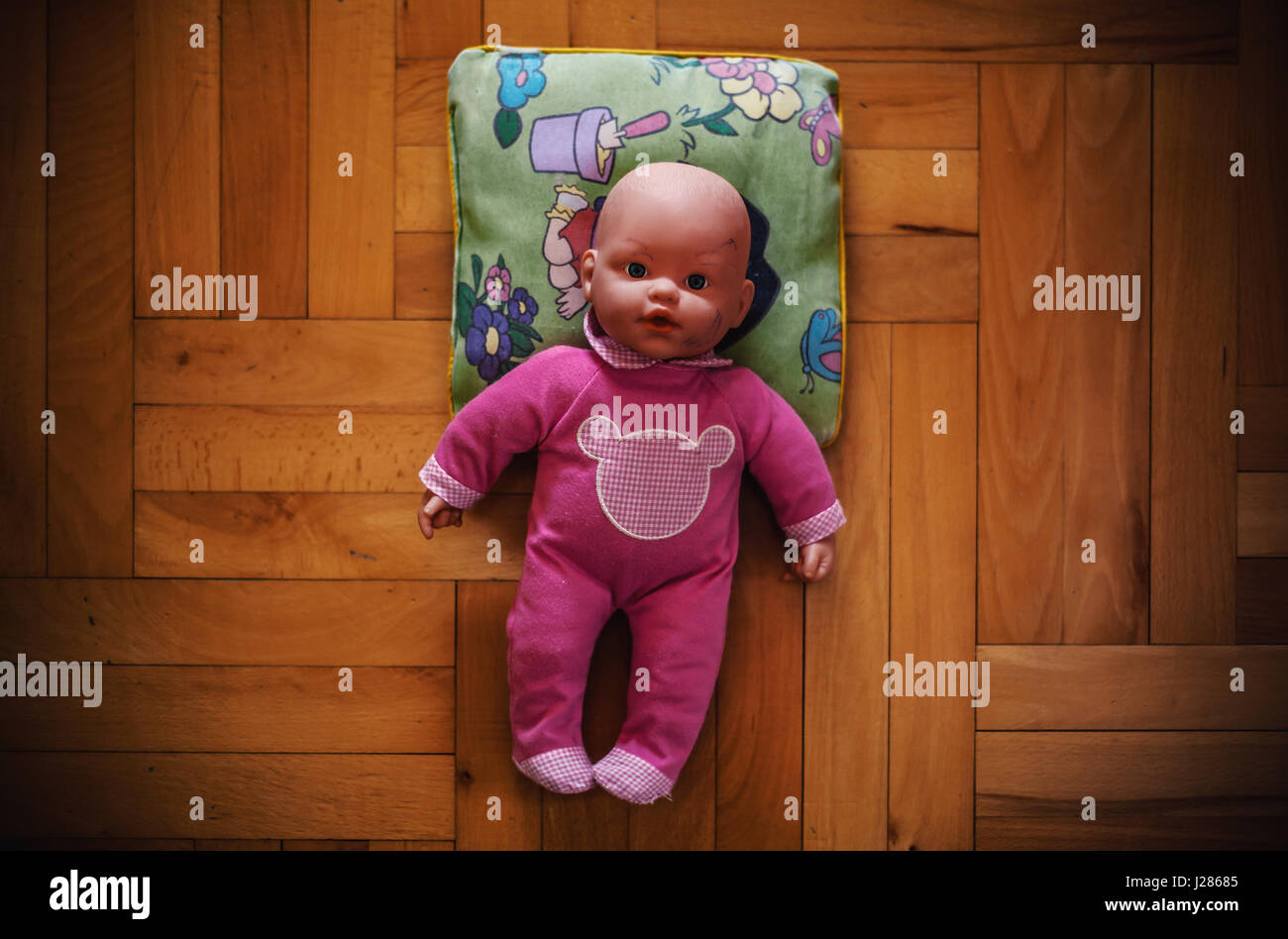Una Baby toy sulle piastrelle del pavimento in legno, in abito rosa posa sul cuscino divertenti. Foto Stock