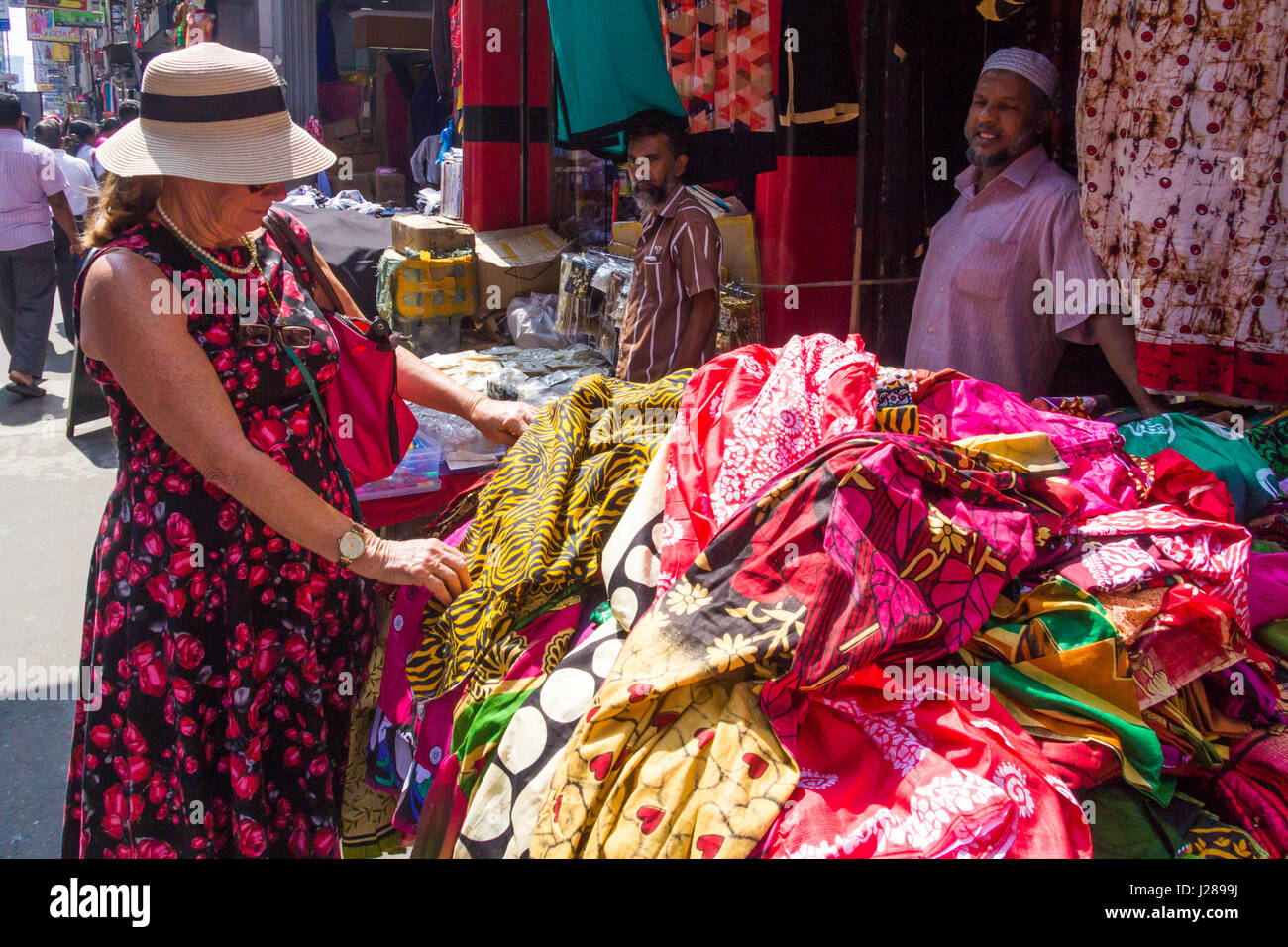 Una donna per turisti in cerca di tessuto su una bancarella di strada nel quartiere di Pettah, Colombo, Sri Lanka Foto Stock