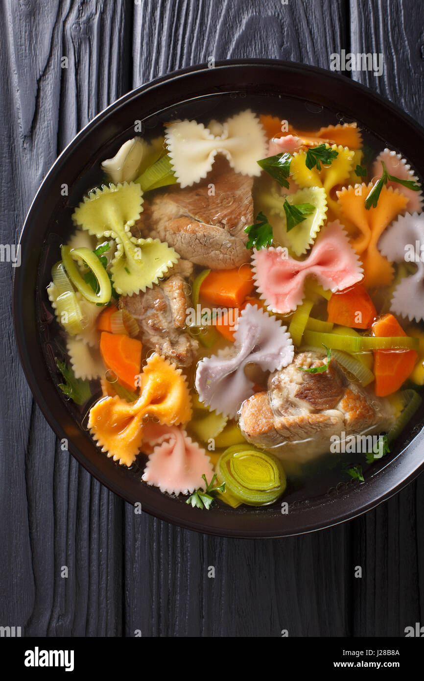 Zuppa italiana con carne di maiale, colorate farfalle di pasta e verdure in una ciotola di close-up. Vista verticale da sopra Foto Stock