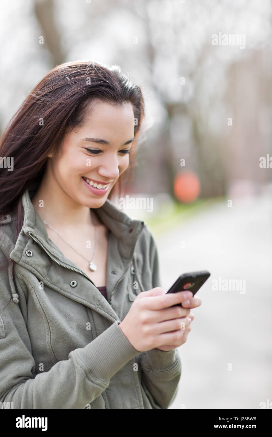 Un colpo di un etnica studente di college texting sul telefono presso il campus Foto Stock