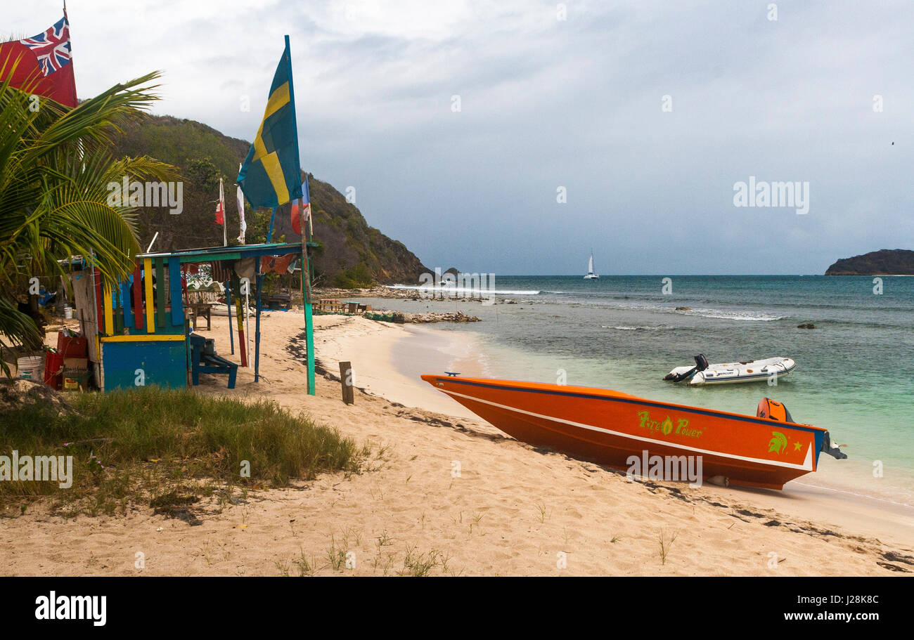 Capanna sulla spiaggia e bandiere internazionali con un taxi d'acqua, spiaggia e vista dei Caraibi: Salt Whistle Bay, Mayreau, Saint Vincent e Grenadine. Foto Stock