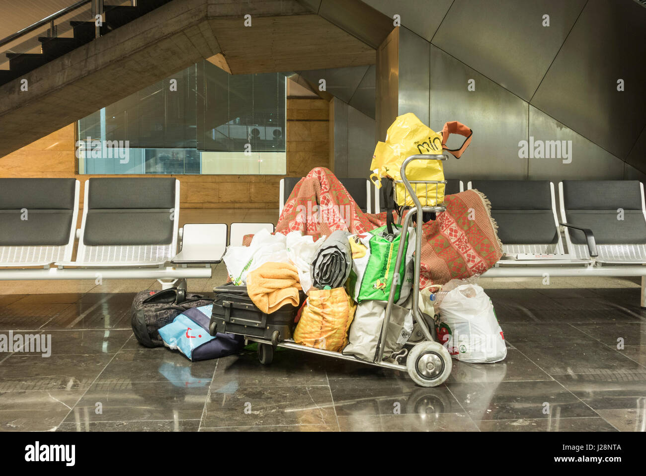 Senzatetto uomo che vive a Gran Canaria aeroporto di dormire su sedili con tutti i suoi possedimenti al aeroporto di trolley. Foto Stock