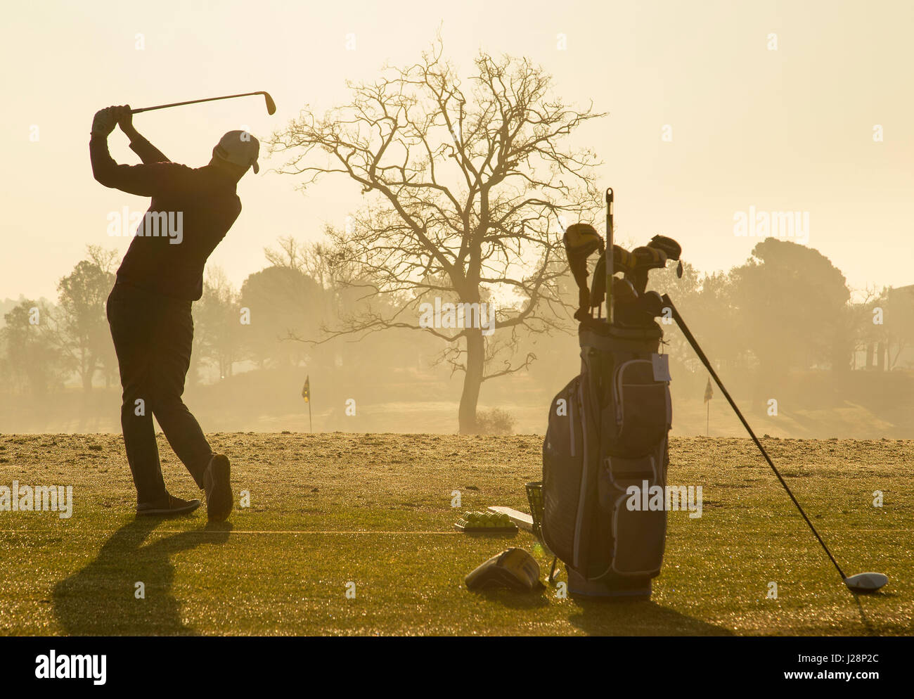 Gli amanti del golf swinging golf club in inizio di mattina di sole su una pratica gamma di guida all'alba. Foto Stock