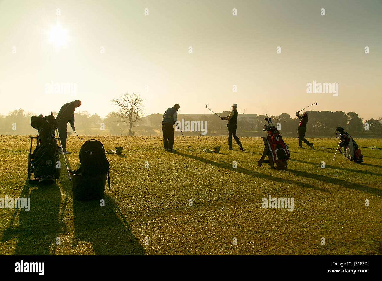 Gli amanti del golf swinging golf club in inizio di mattina di sole su una pratica gamma di guida all'alba. Foto Stock