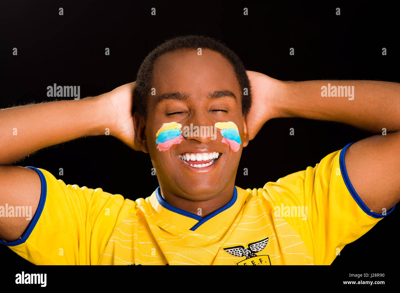 Quito, Ecuador - 25 Maggio 2016: Headshot dark scuoiati maschio giallo da indossare ecuadoriano football shirt davanti a sfondo nero, bandiera vernice per il viso, rivolto verso la fotocamera e il tifo con entusiasmo Foto Stock