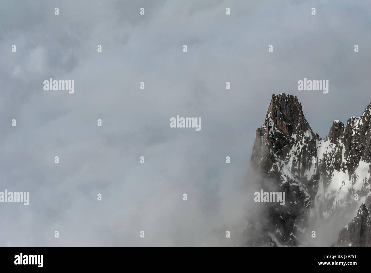Cima di una montagna scogliera che si estende dal crinale fuoriuscente attraverso grigia spessa copertura nuvolosa Foto Stock