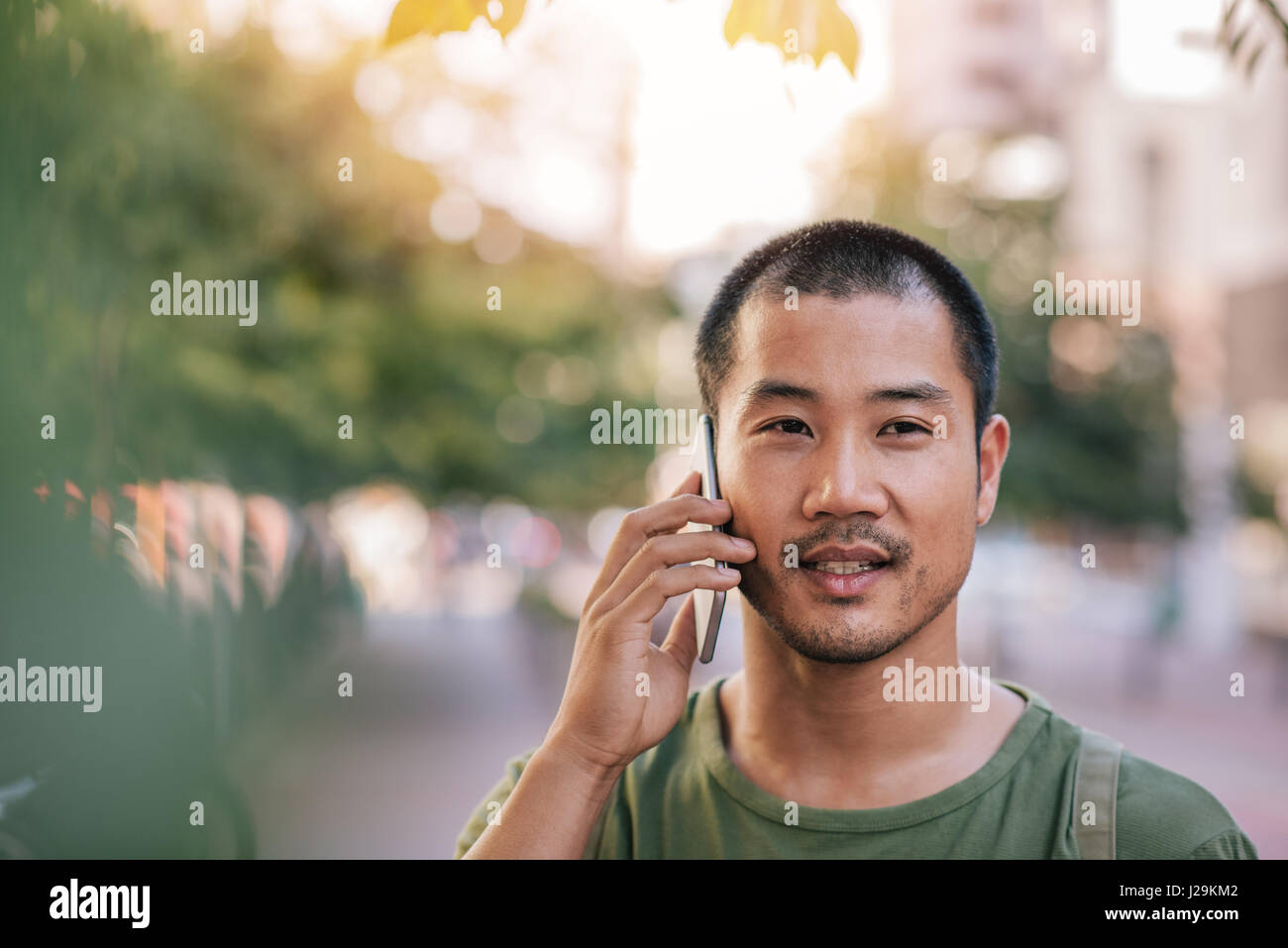 Giovane uomo asiatico parlando sul suo cellulare al di fuori Foto Stock