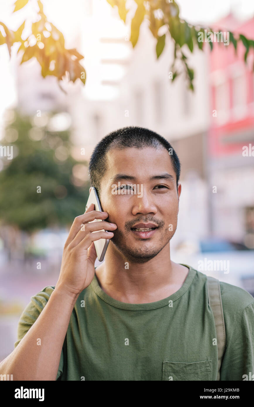 Giovane uomo asiatico avente una conversazione sul suo cellulare al di fuori Foto Stock