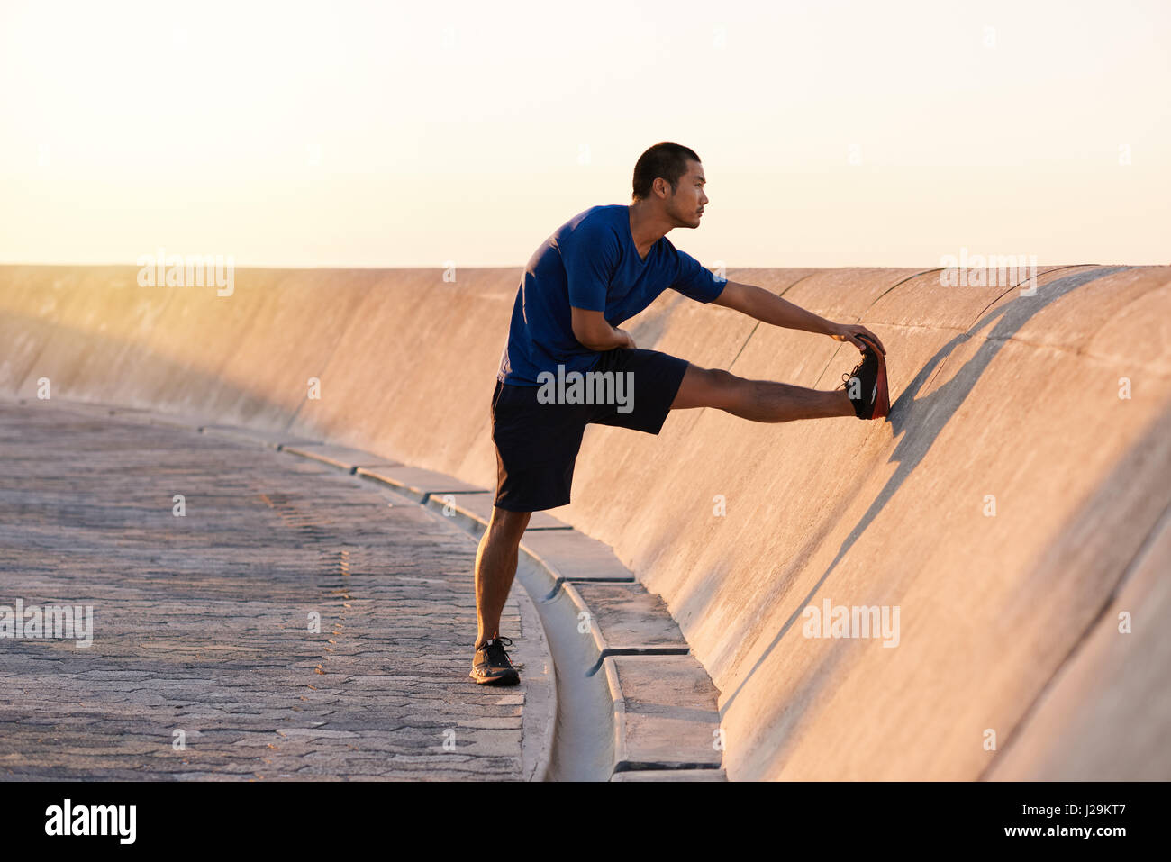 Atletica Giovane uomo asiatico stretching le sue gambe prima di una corsa Foto Stock