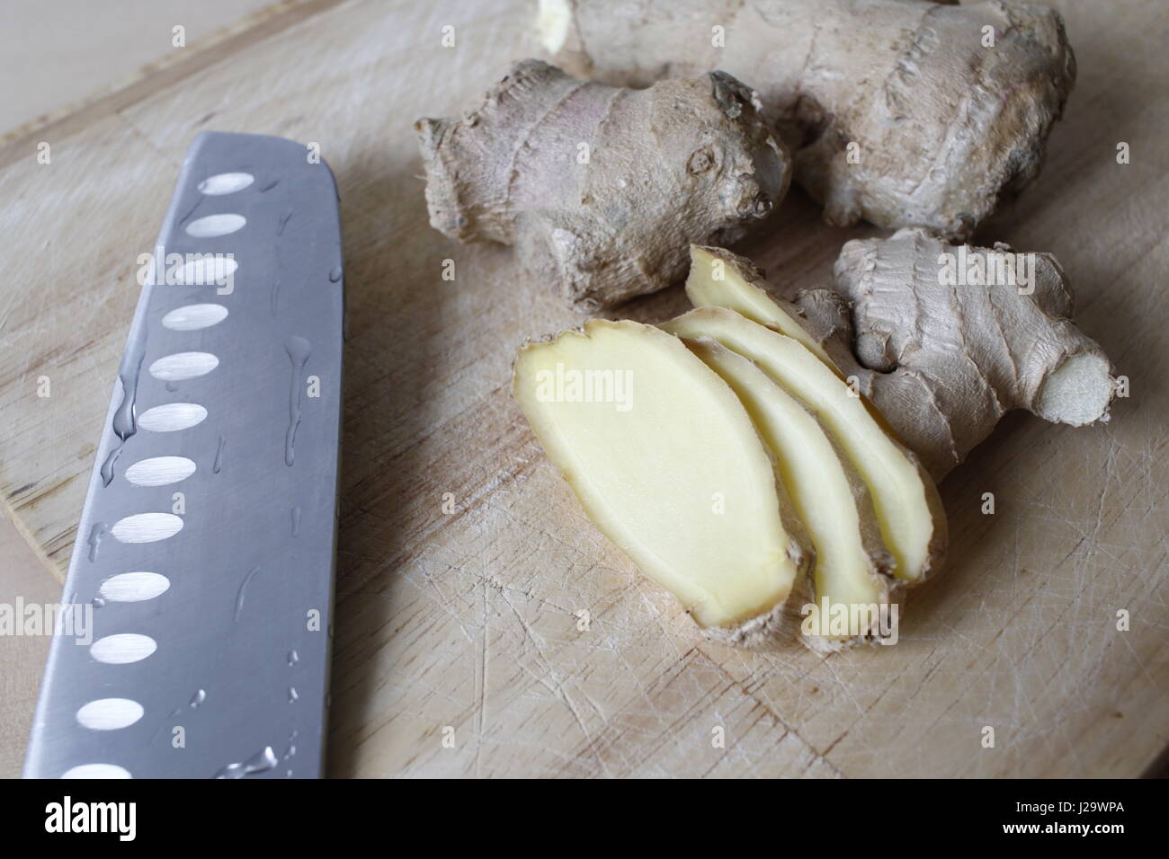 Pezzi di radice di zenzero su un piatto di legno con un coltello oltre a loro. Foto Stock