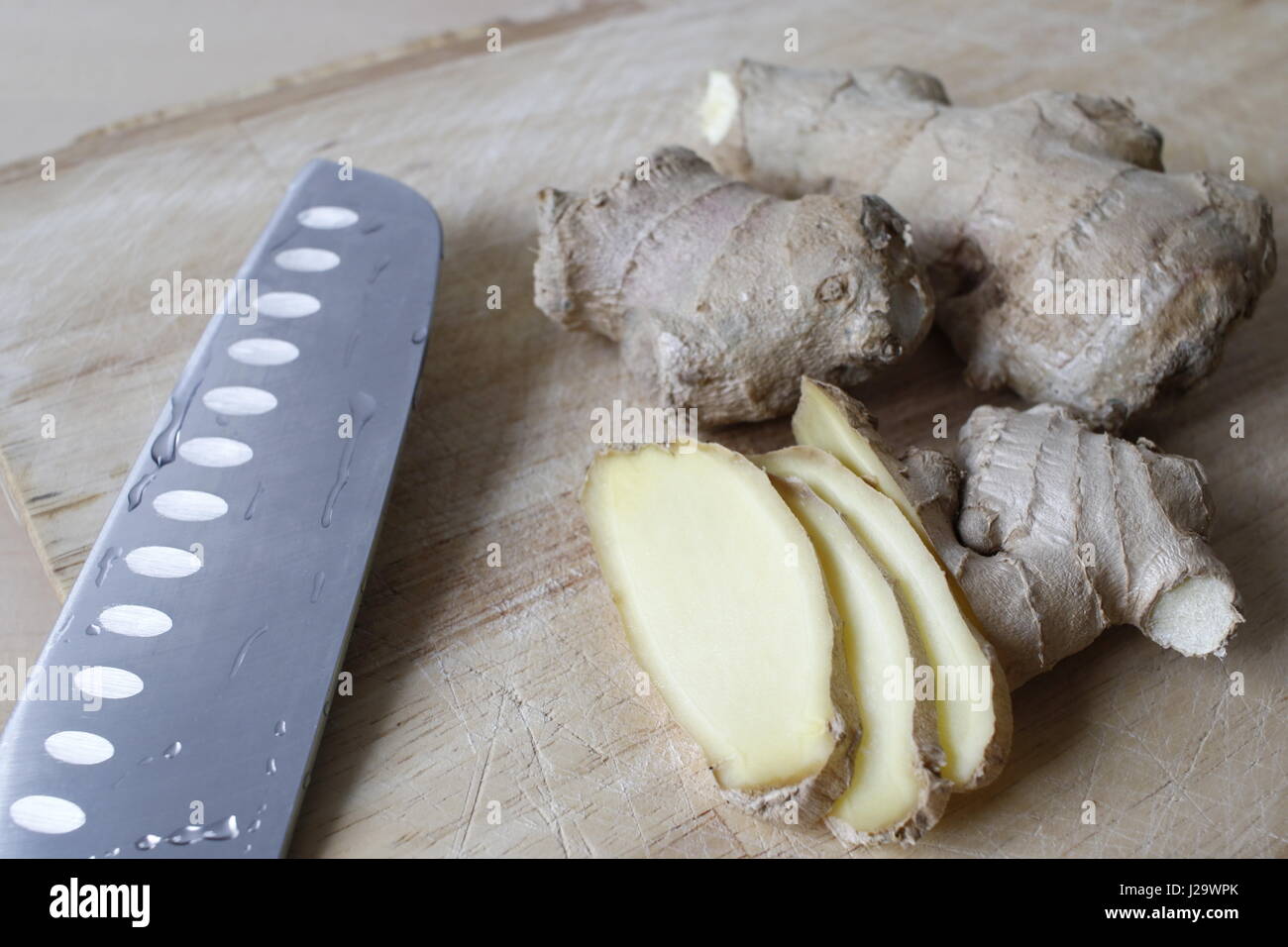 Pezzi di radice di zenzero su un piatto di legno con un coltello oltre a loro. Foto Stock