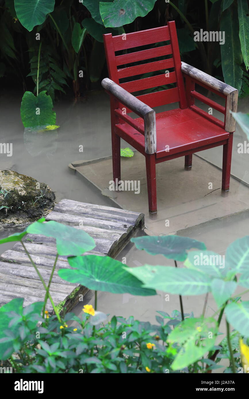 Maroon di legno verniciato poltrona posizionato nel mezzo di acqua e collegata a terra attraverso una pista di log che serve come pesce spa. Parco delle Farfalle in co Foto Stock