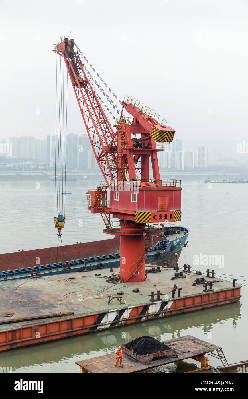 Cina, Chongqing, lavoratore badili polvere di carbone sotto enormi gru nel terminale di carico lungo il fiume Yangtze sul pomeriggio autunnale Foto Stock