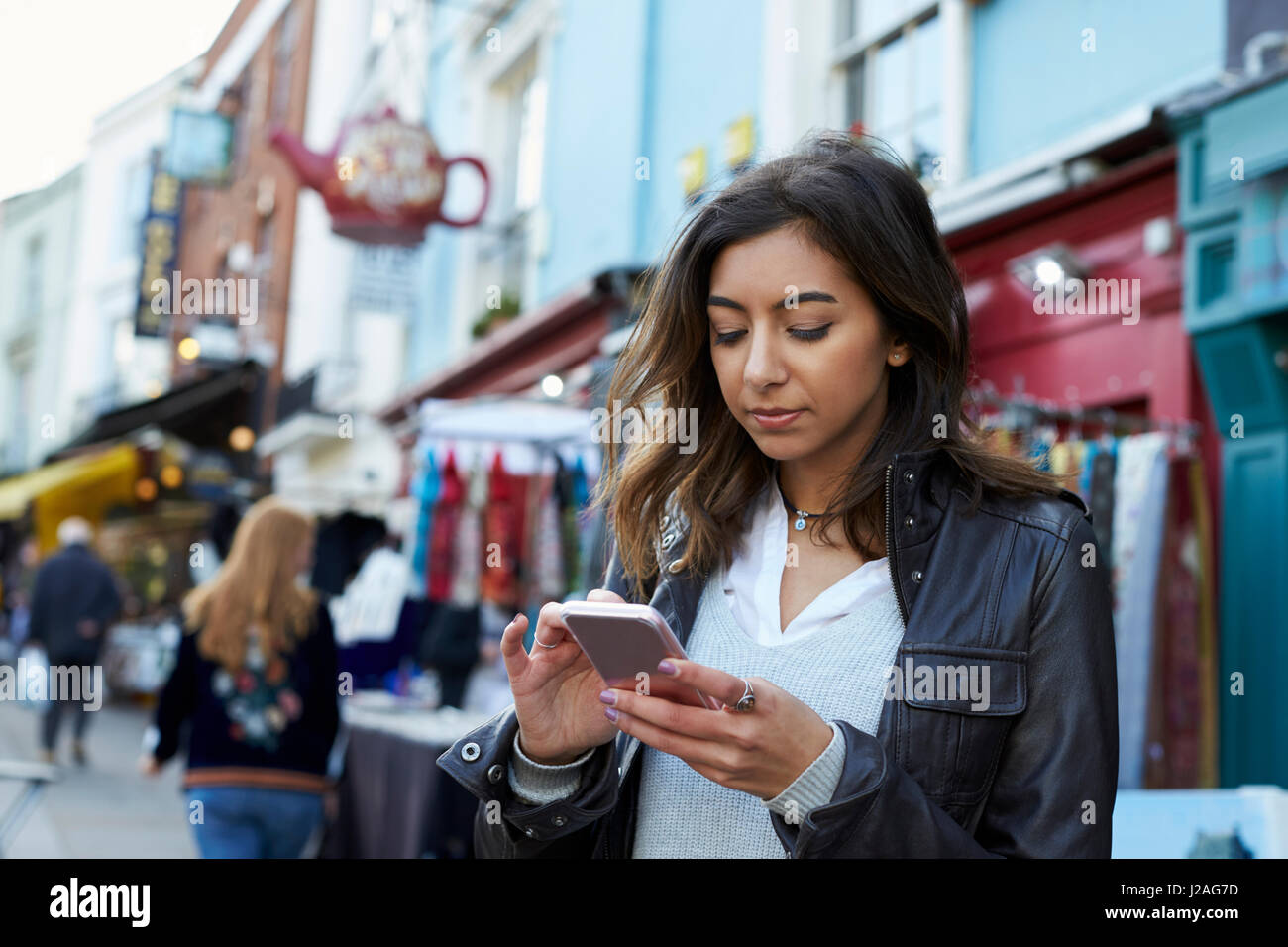 Giovane donna usando il telefono nel mercato di Portobello Road, vicino fino Foto Stock