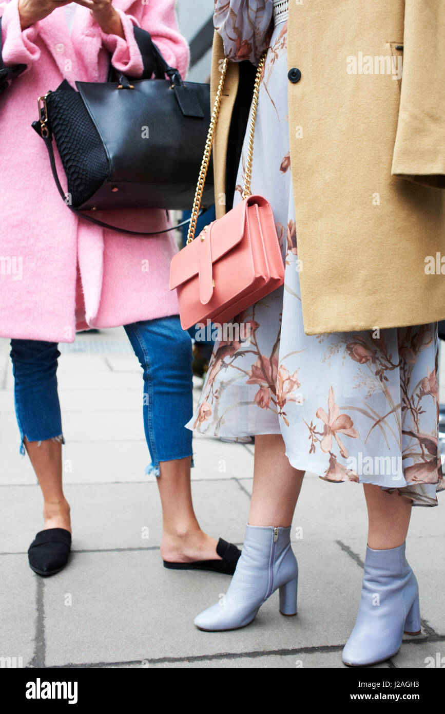 Londra - febbraio, 2017: sezione bassa di due donne alla moda in piedi in strada indossano tuniche e designer borsette, Valentino sacchetto sulla sinistra, London Fashion Week, verticale, vista frontale Foto Stock
