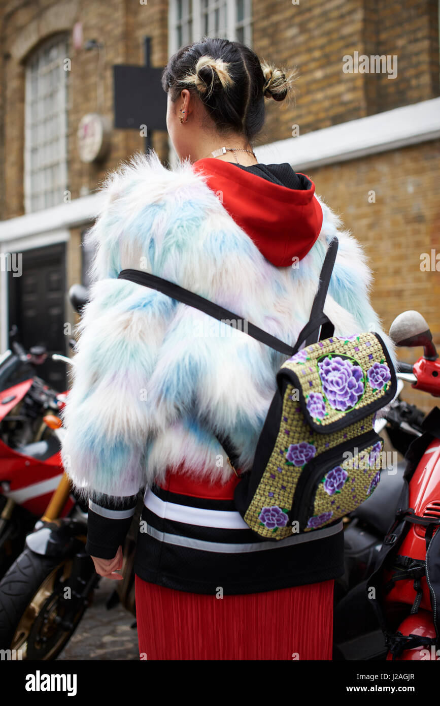 Londra - febbraio, 2017: Moda giovane donna che indossa la pelliccia finta camicia al di sopra hoodie con uno zaino sulla schiena in piedi in strada durante la London Fashion Week, verticale Foto Stock