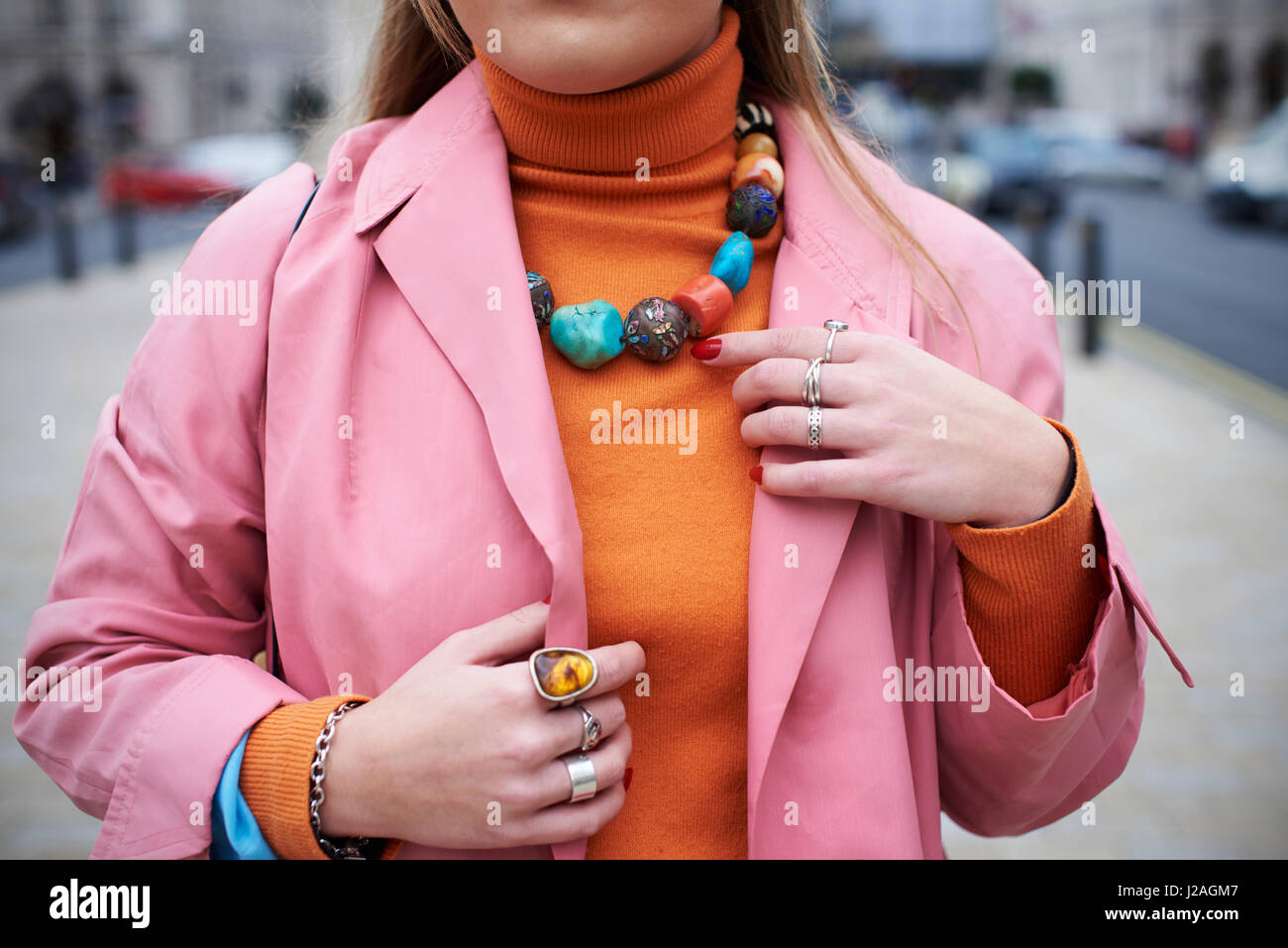 Londra - febbraio, 2017: sezione centrale della donna che indossa cappotto rosa e arancio felpa con chunky collana in pietra e gli anelli in piedi in una strada durante la London Fashion Week, orizzontale Foto Stock