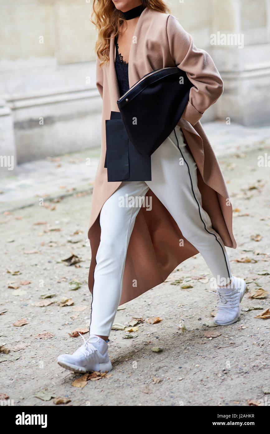 La donna che indossa a piedi lungo cappotto e pantaloni bianchi, il raccolto Foto Stock