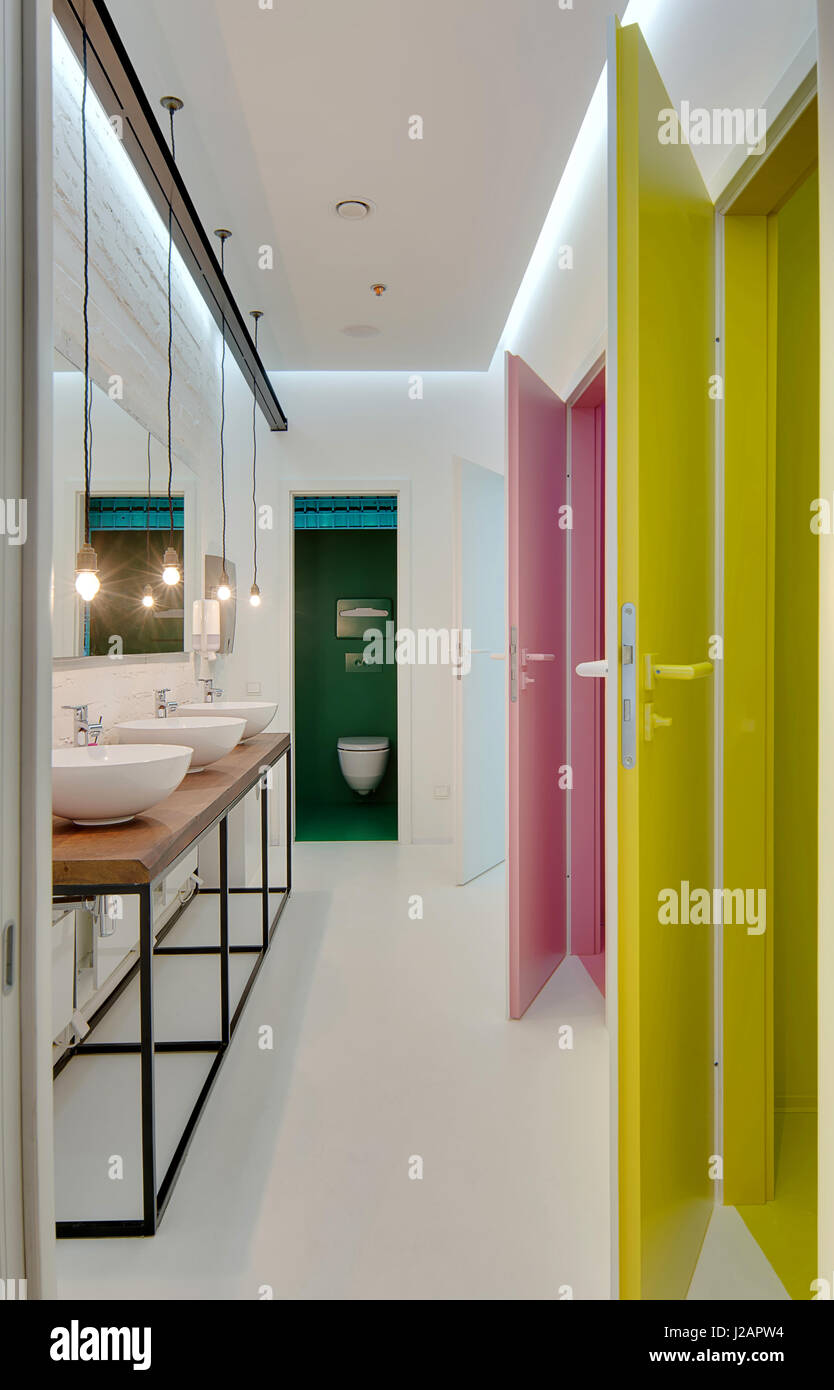 Restroom luminosa con pareti bianche e multi-porte color: ciano, rosa,  giallo. Vi è un rack in legno con tre lavandini, specchio sopra di essi  appesi a Lam Foto stock - Alamy