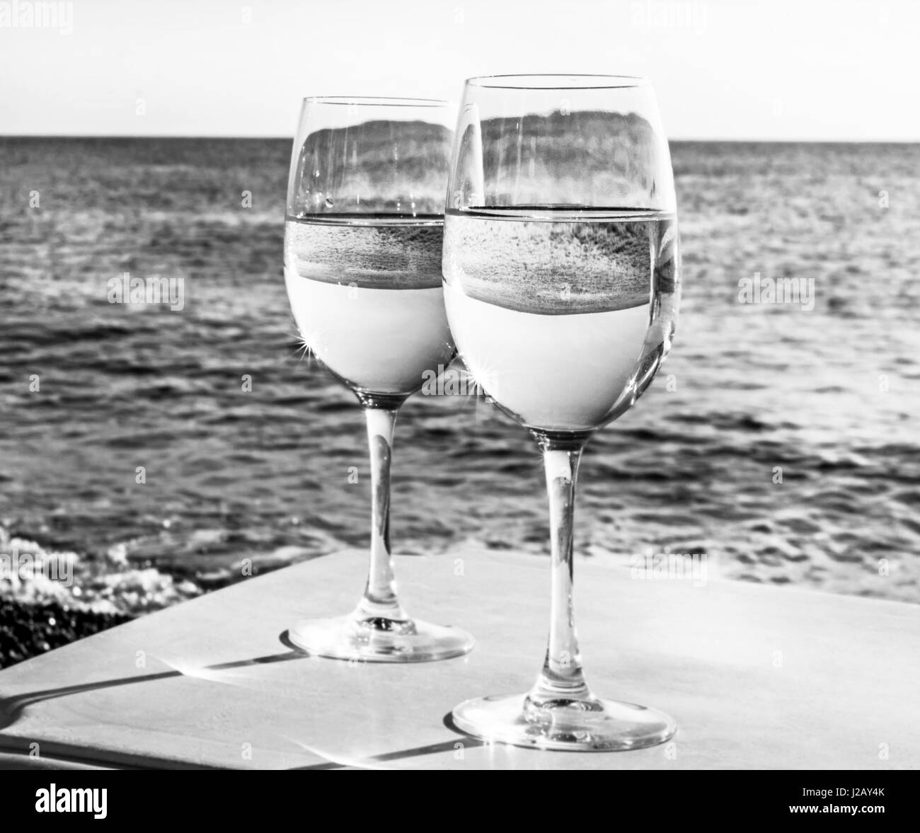 Due bicchieri di vino sulla spiaggia vicino oceano al giorno in bianco e nero Foto Stock