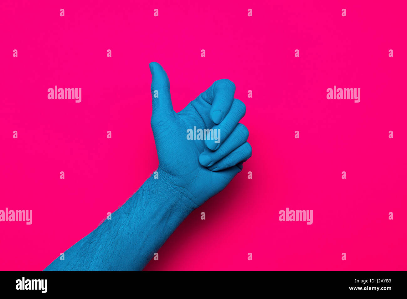 Close-up di blu dipinto a mano pollice gesti fino contro sfondo rosa Foto Stock