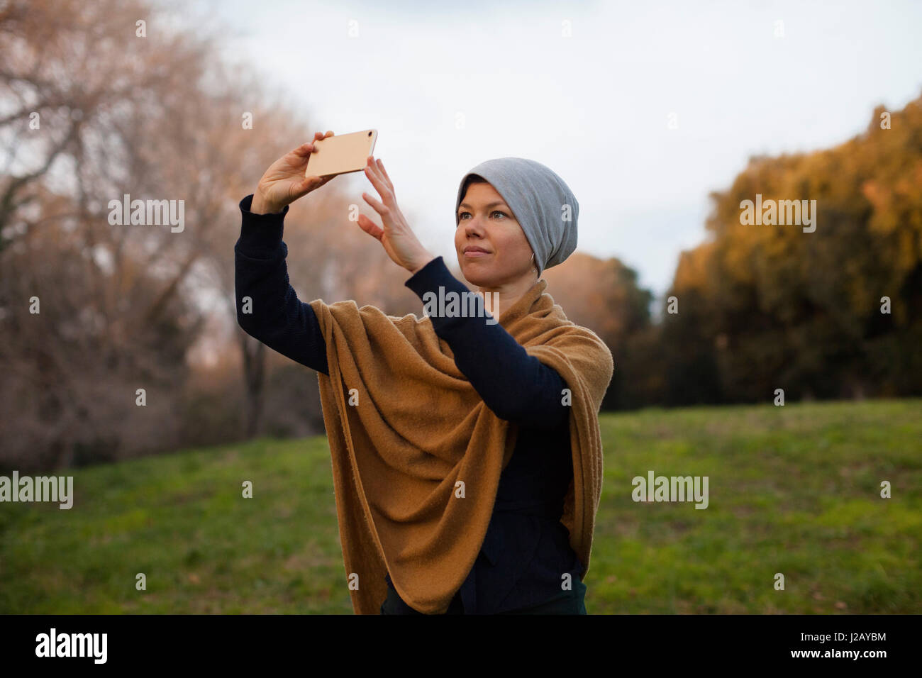 Metà donna adulta fotografando attraverso smart phone sul campo contro sky Foto Stock