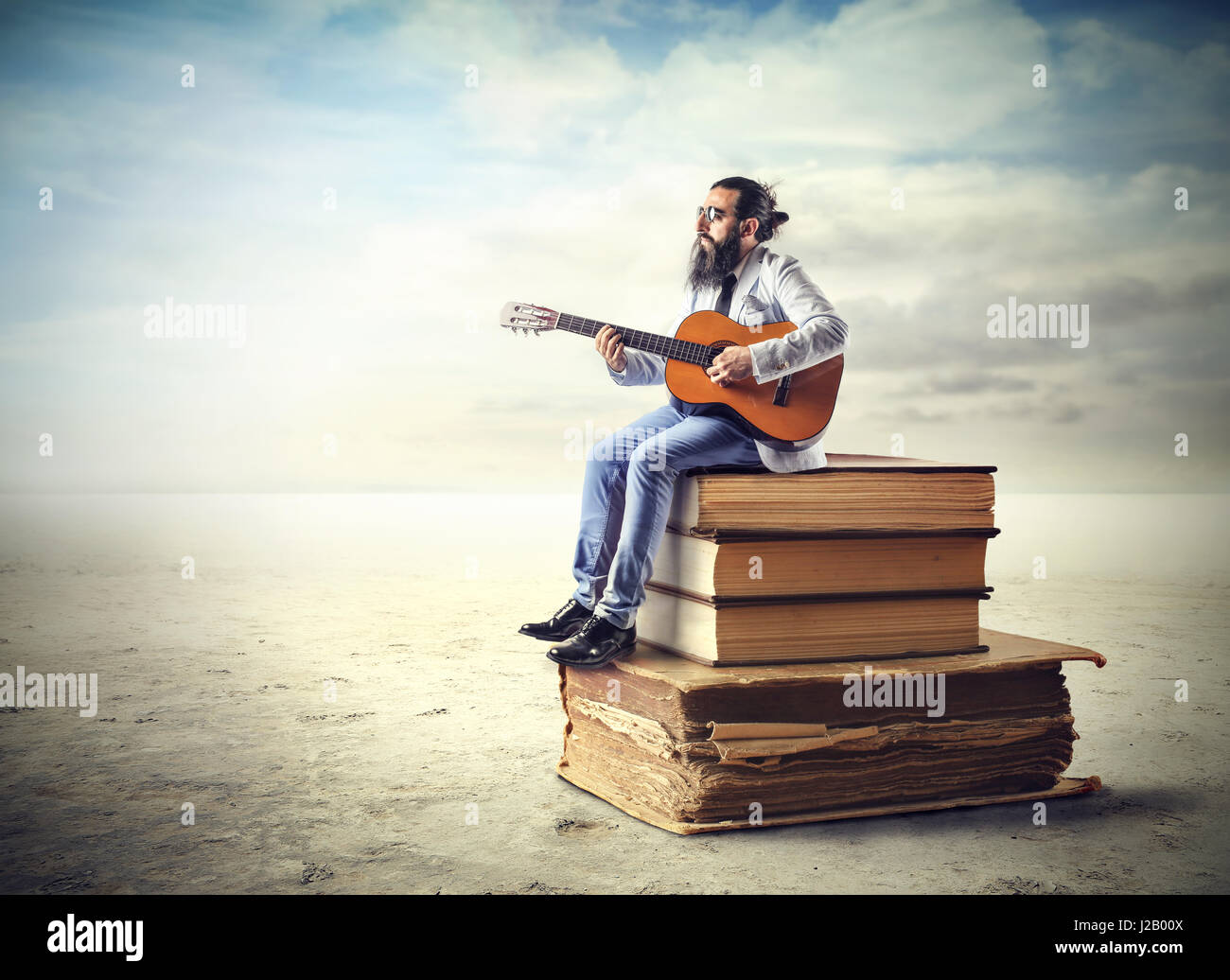 L'uomo con la chitarra seduto su un enorme libri Foto Stock