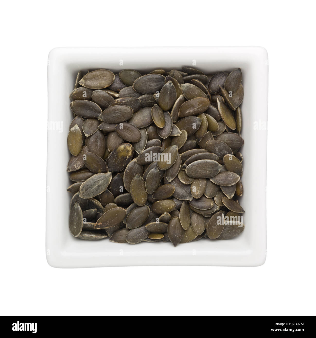 I semi di zucca in un recipiente quadrato isolato su sfondo bianco Foto Stock