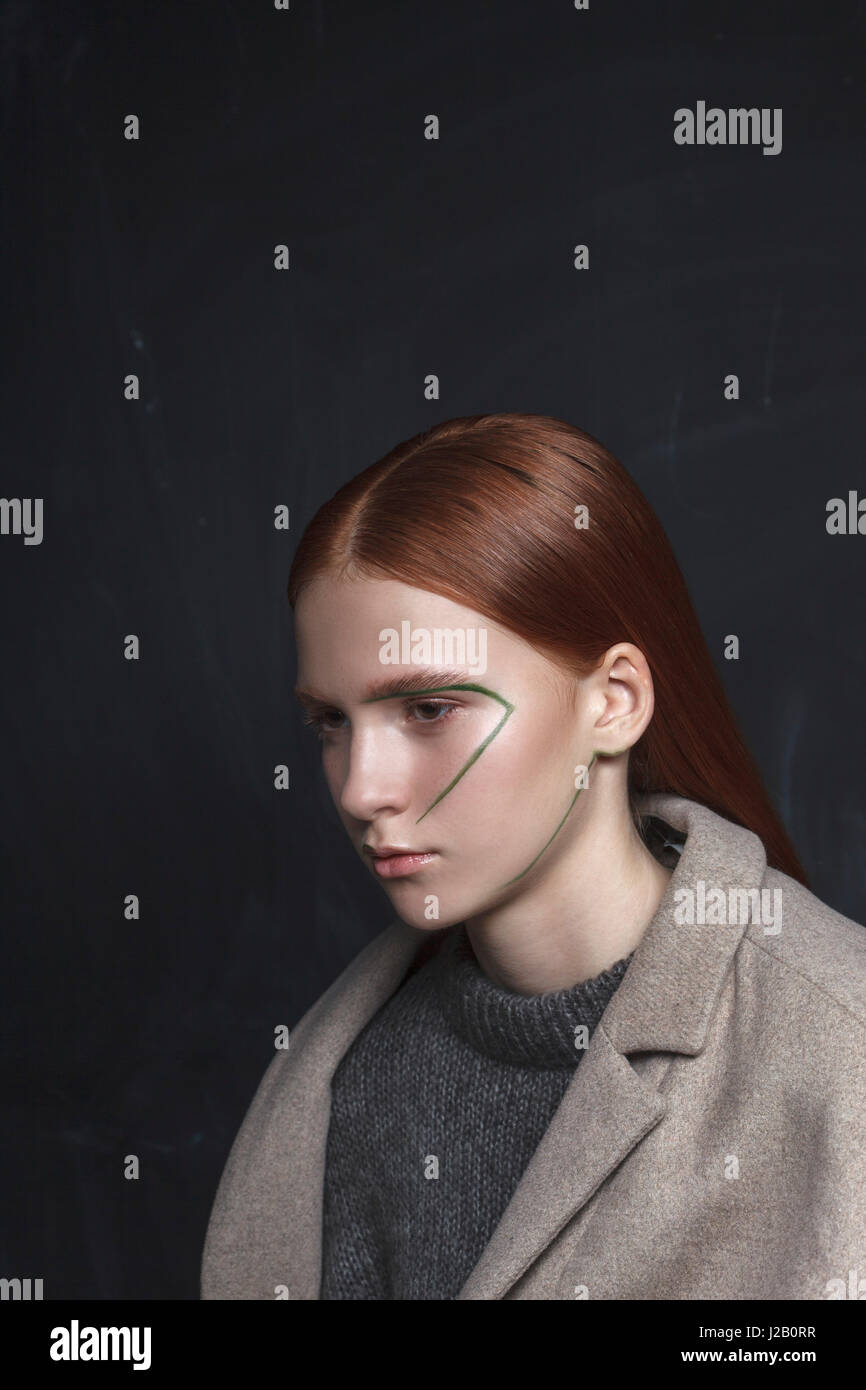 Premurosa ragazza adolescente in giacca con faccia vernice contro lo sfondo nero Foto Stock