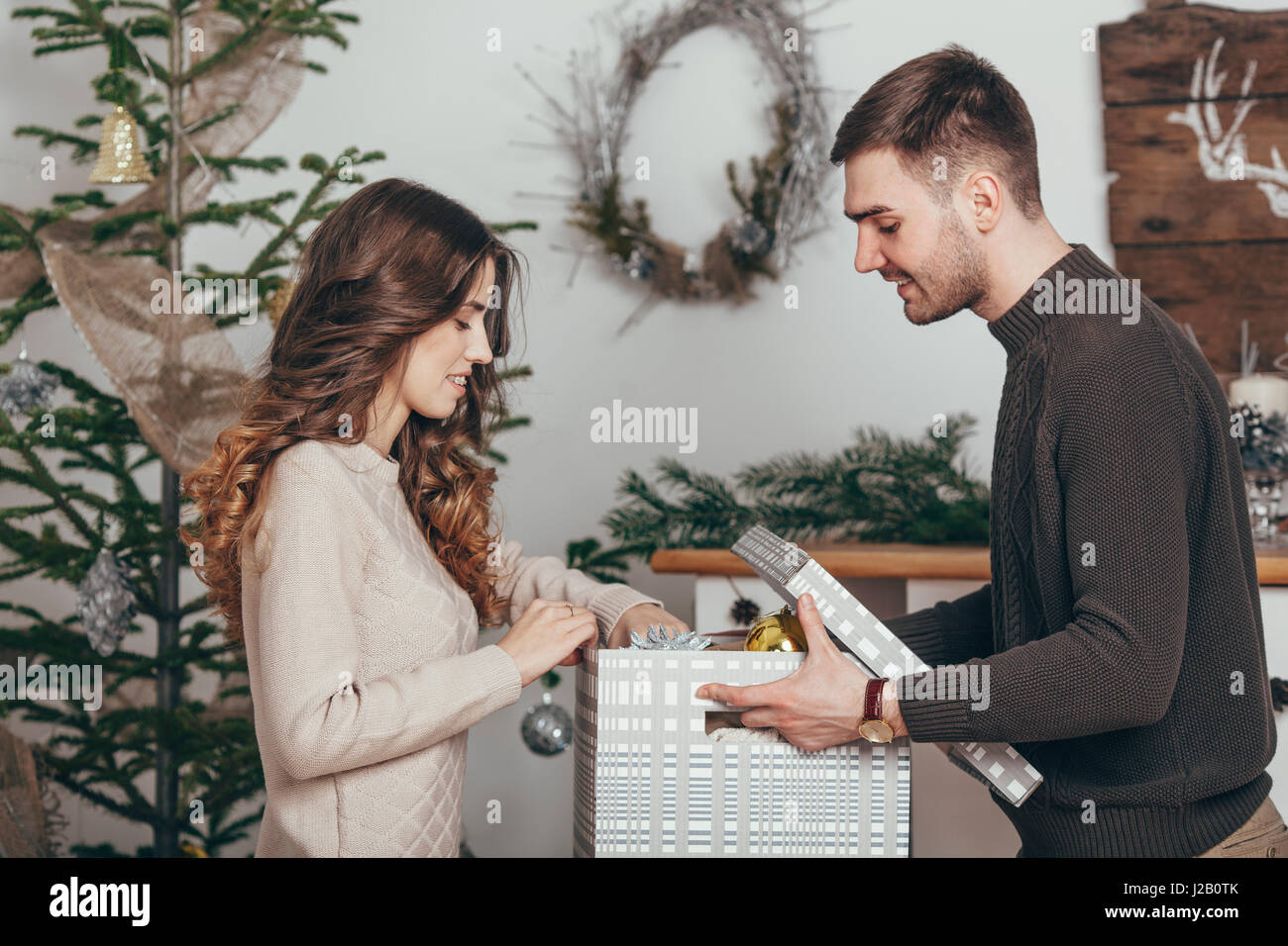 Vista laterale della coppia sorridente imballaggio regali di Natale a casa Foto Stock