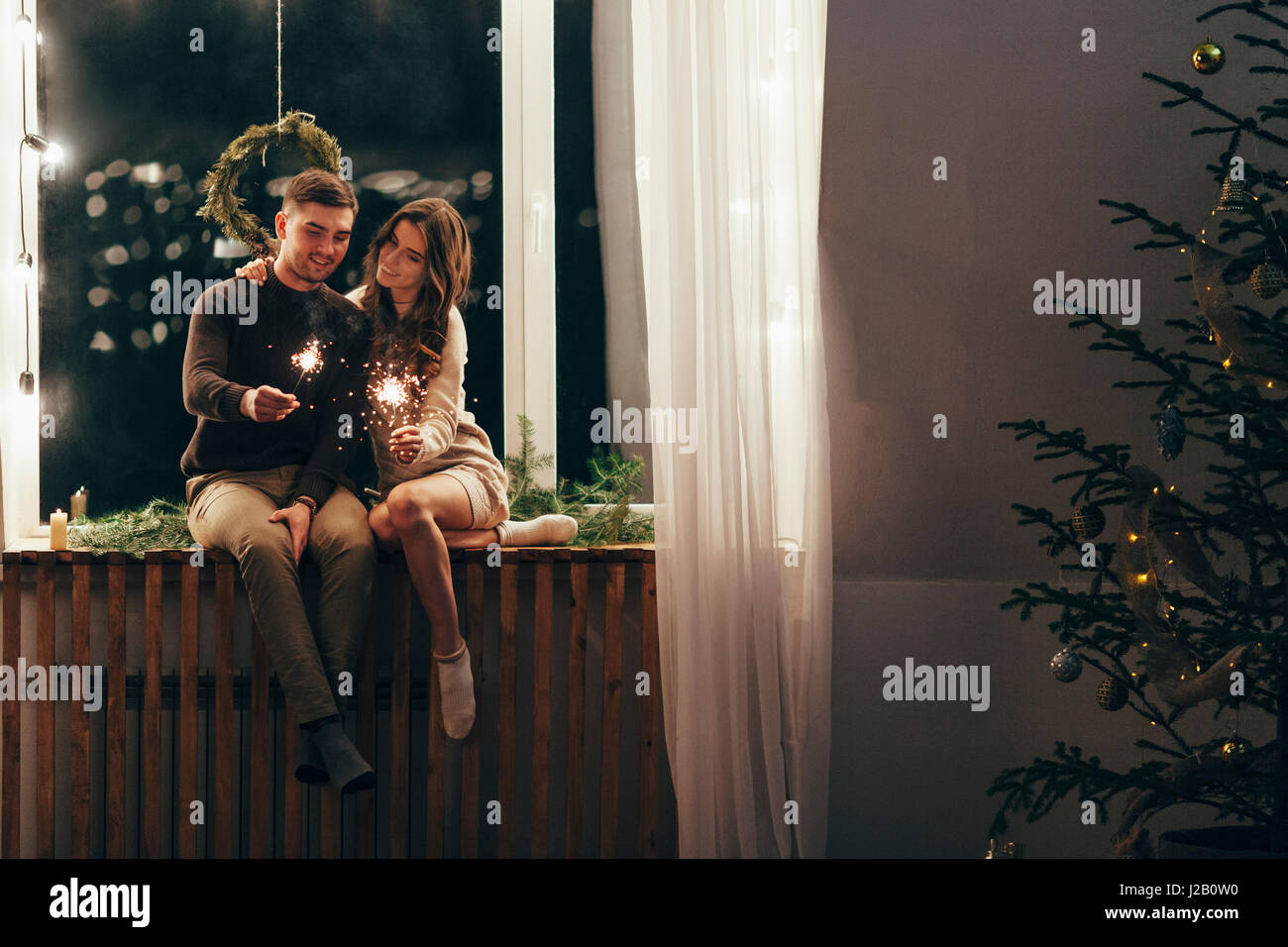 Coppia felice giocando con botti mentre è seduto sul davanzale durante il periodo di Natale Foto Stock