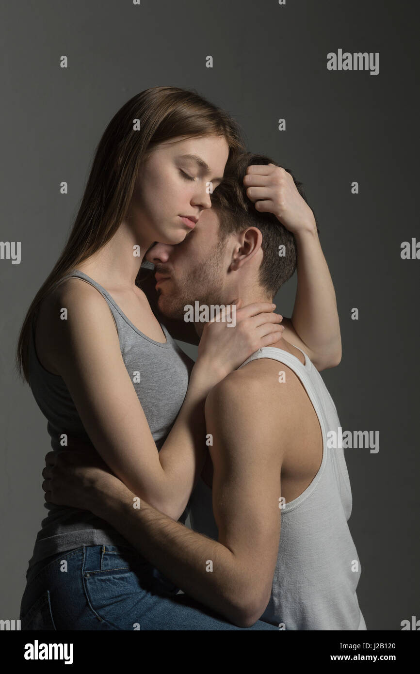 Amare giovane abbracciando contro uno sfondo grigio Foto Stock