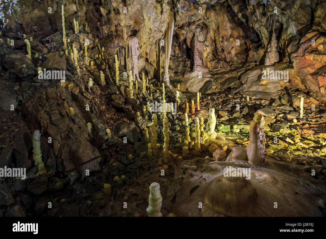 Grotta con colorate pareti ruvide e stalattiti e stalagmiti illuminato da dietro Foto Stock