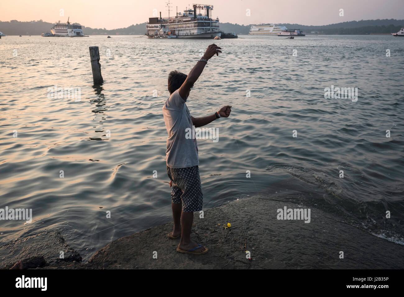 Un pescatore cerca di catturare un pesce di fronte a una delle barche usate come un casino in Panjim Foto Stock