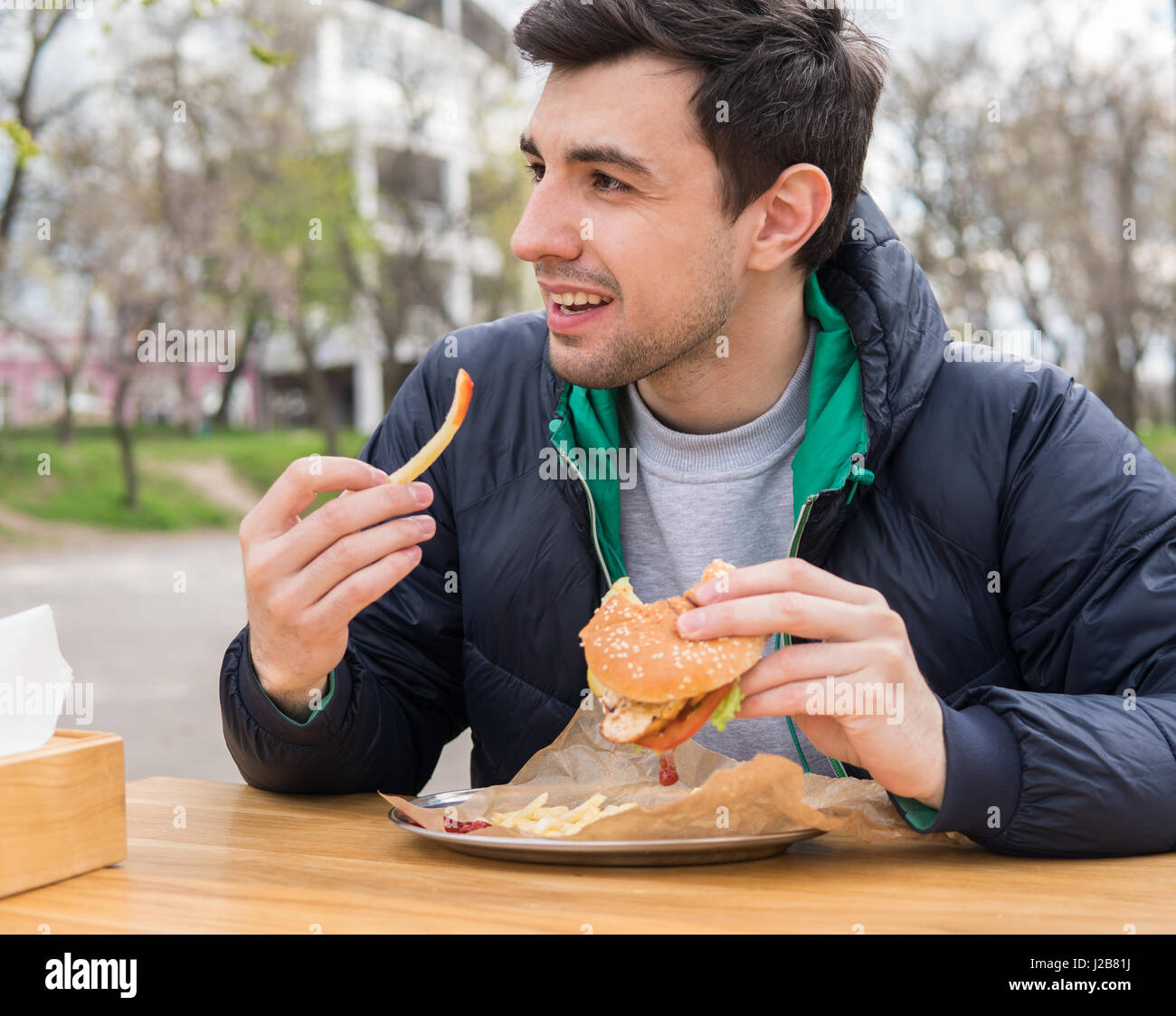 Uomo di mangiare un hamburger con patatine fritte in street food cafe Foto Stock