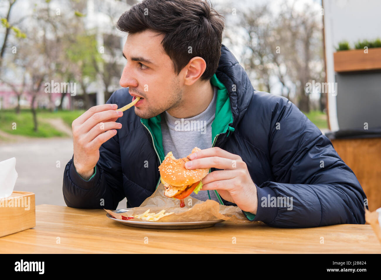 L'uomo mangiare patate fritte con un hamburger in street food cafe Foto Stock