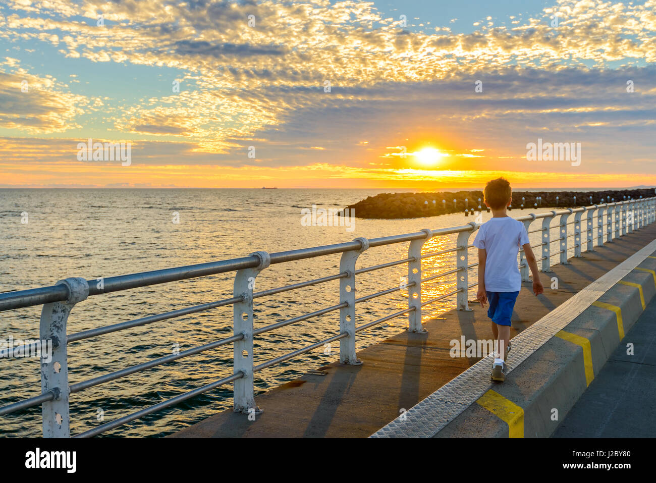 Ragazzo camminando lungo St Kilda molo al tramonto, Melbourne, Victoria, Australia Foto Stock