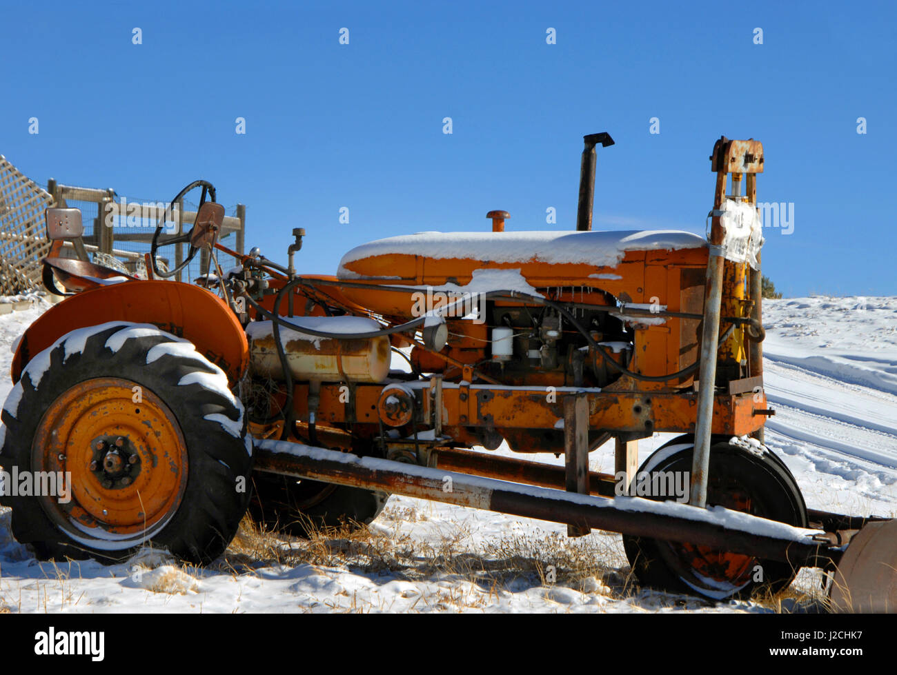 Arancione Il trattore si trova all'aperto in condizioni atmosferiche. La neve si siede su pneumatici e il cofano. Spazzaneve è allegata. Foto Stock
